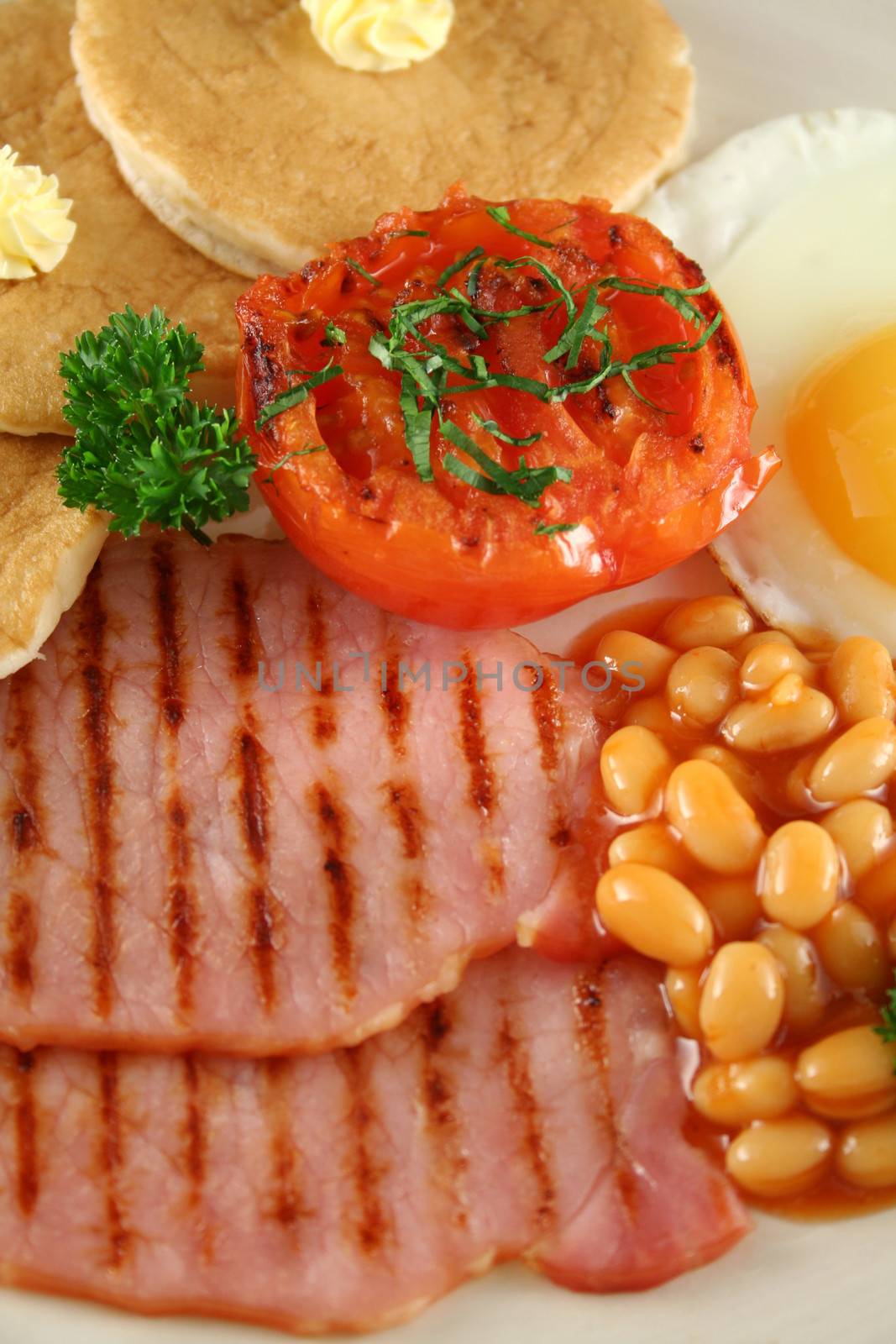 Breakfast of grilled bacon, tomato, egg, baked beans and pancakes.