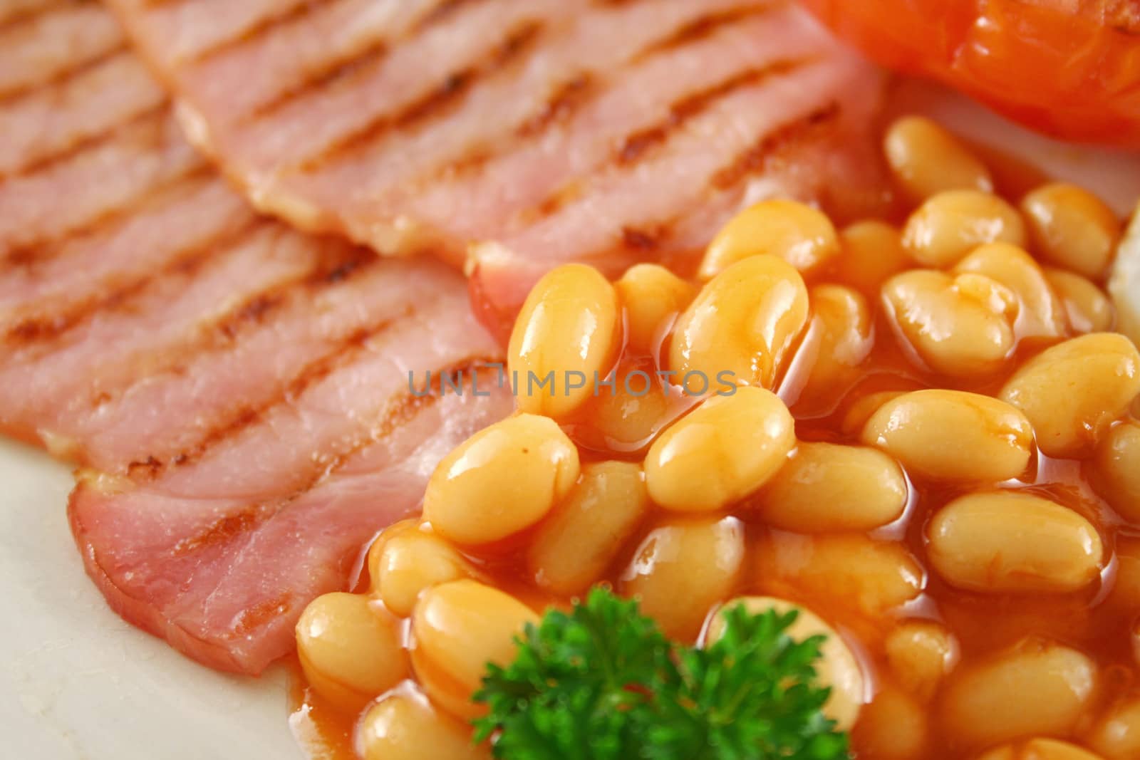 Breakfast of grilled bacon, tomato, egg and baked beans.