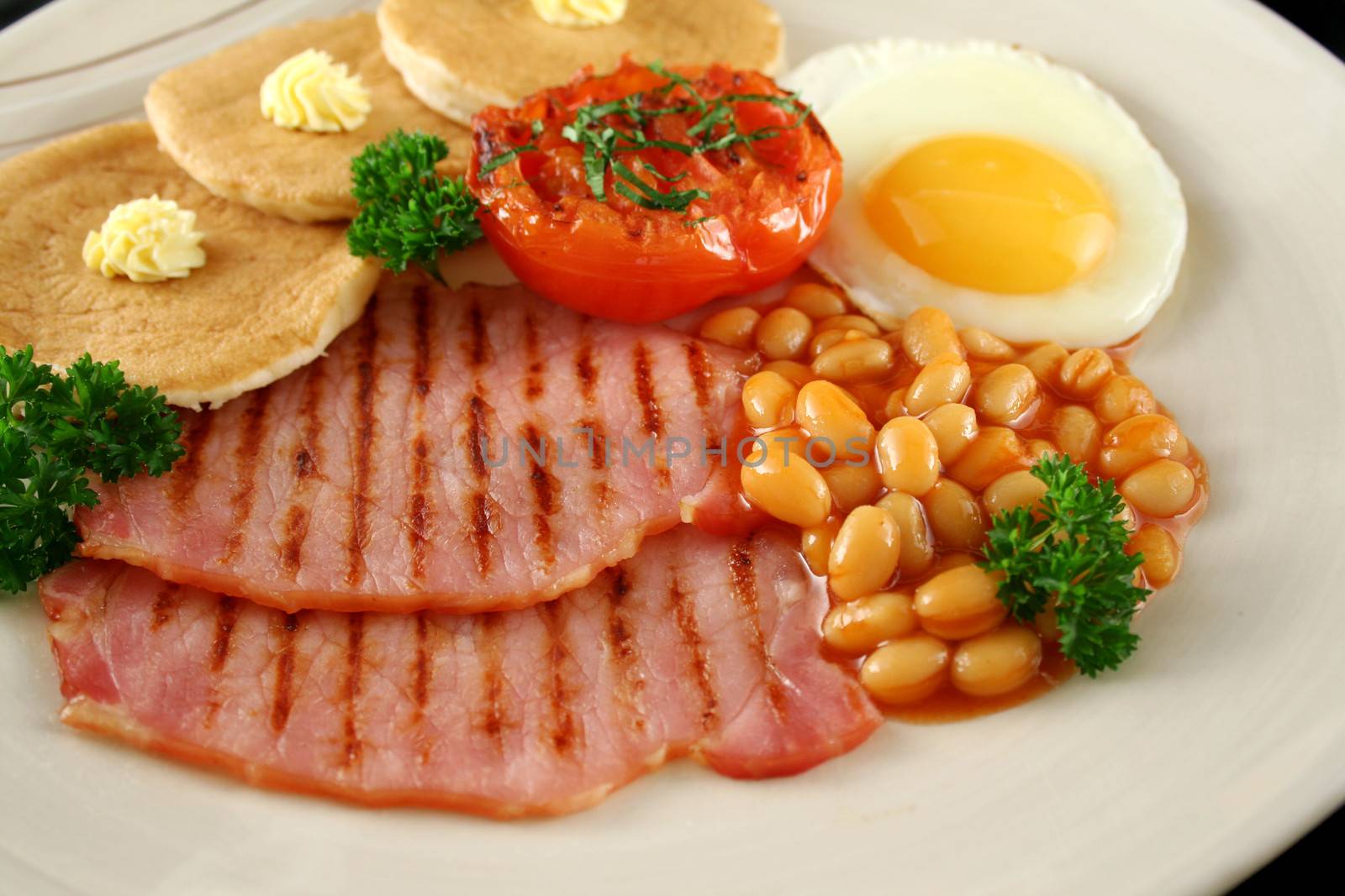 Breakfast of grilled bacon, tomato, egg, baked beans and pancakes.