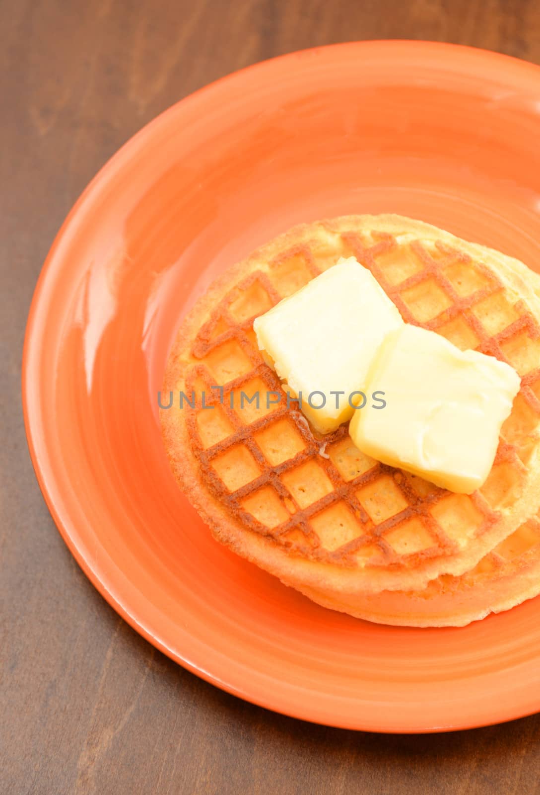 two classic waffles with butter on orange plate and wood
