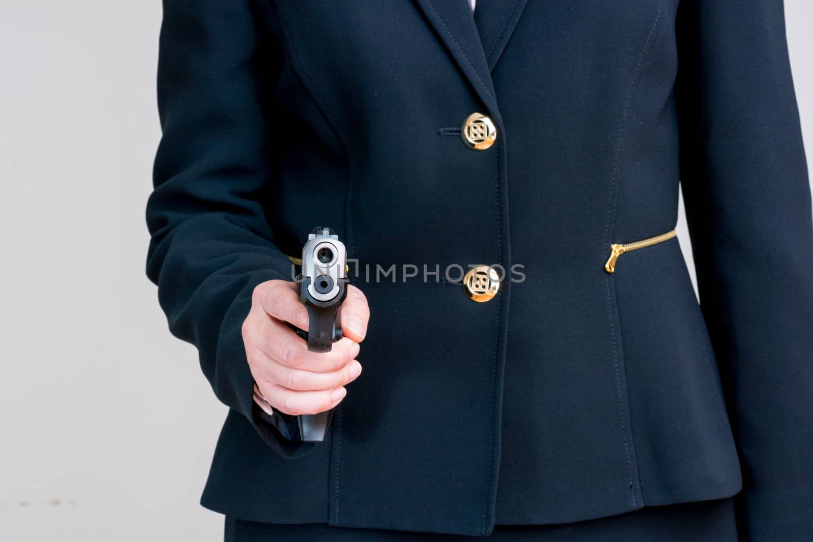 Close up of woman in business suit pointing a hand gun at you  on gray background