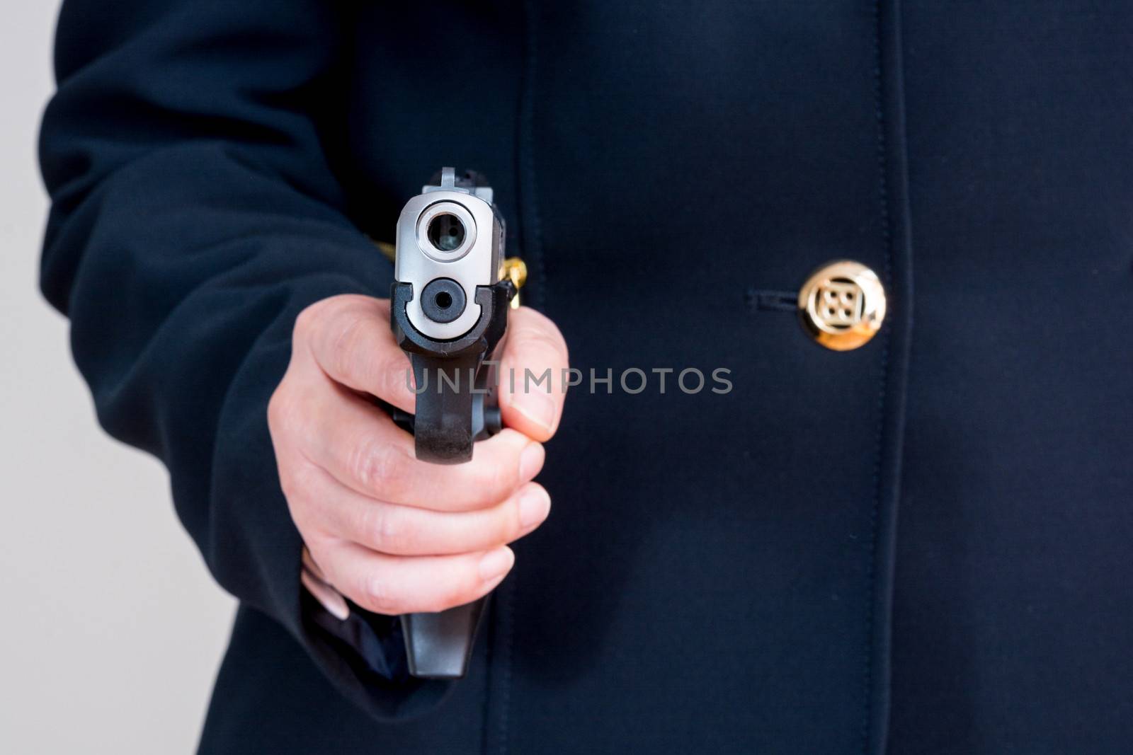 Close up of woman in business suit pointing a hand gun at you  on gray background