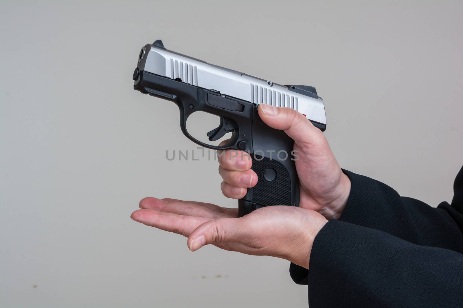 Close up of woman in business suit loading a pistol on gray background