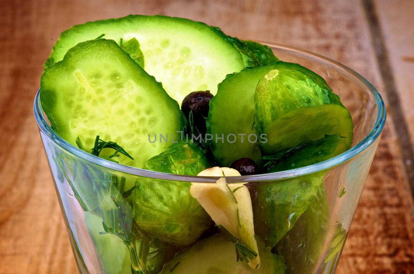 Appetizer with Slices of Delicious Pickled Cucumbers in Brine of Garlic, Dill, Parsley and Black Peppercorn in Glass Dish closeup on Wooden background