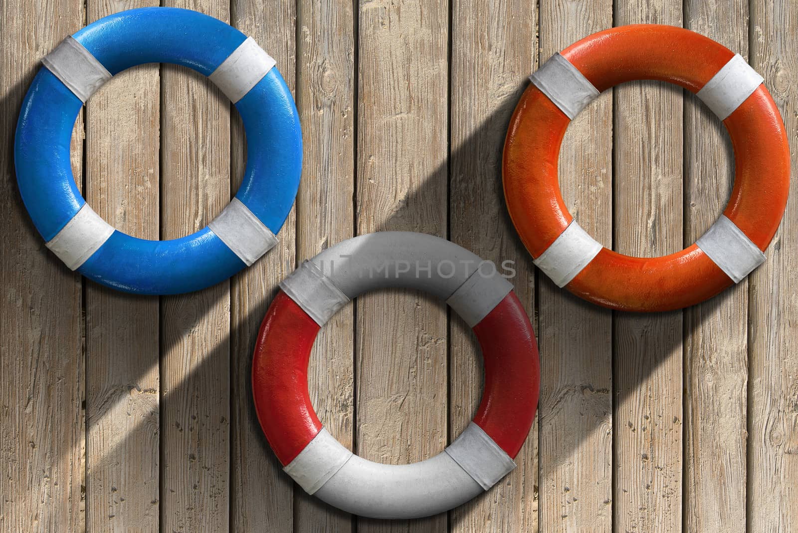 Three lifebuoys hanging to a wooden wall with sand and shadows
