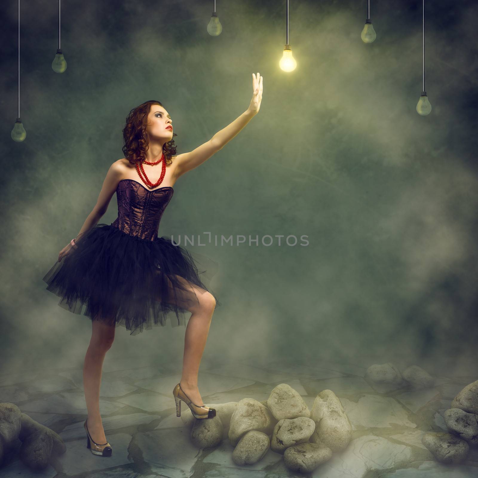 young woman holds up a hand to a glowing light bulb