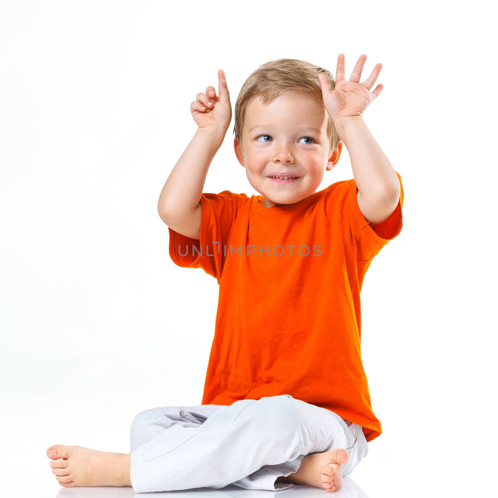 Adorable happy boy sitting on the floor in studio. Isolated of white background.