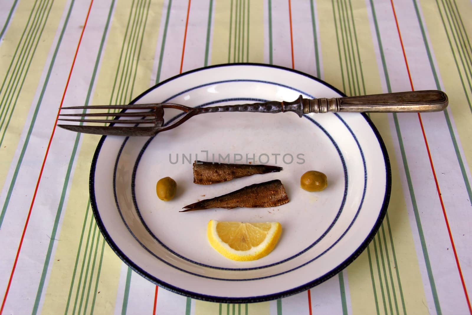fork with knife on dish with olive, fish  and lemon