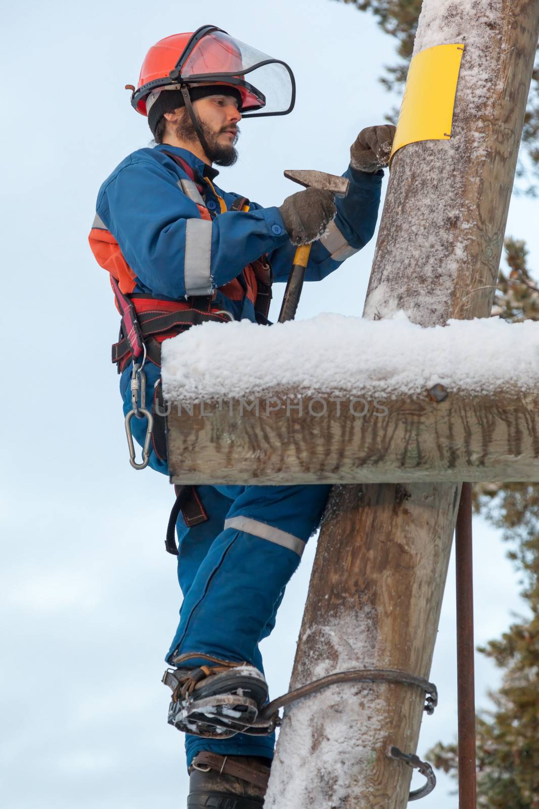 Electrician in blue overalls working on a power line pole in winter