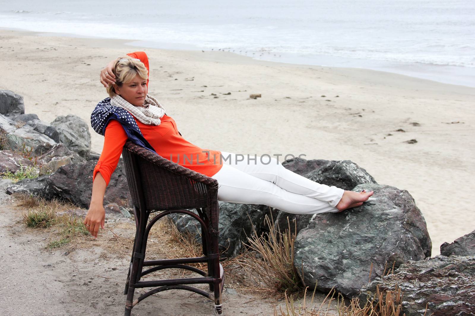 Side view of adult woman looking away while sitting on a wooden chair at grassy beach Half moon bay. California