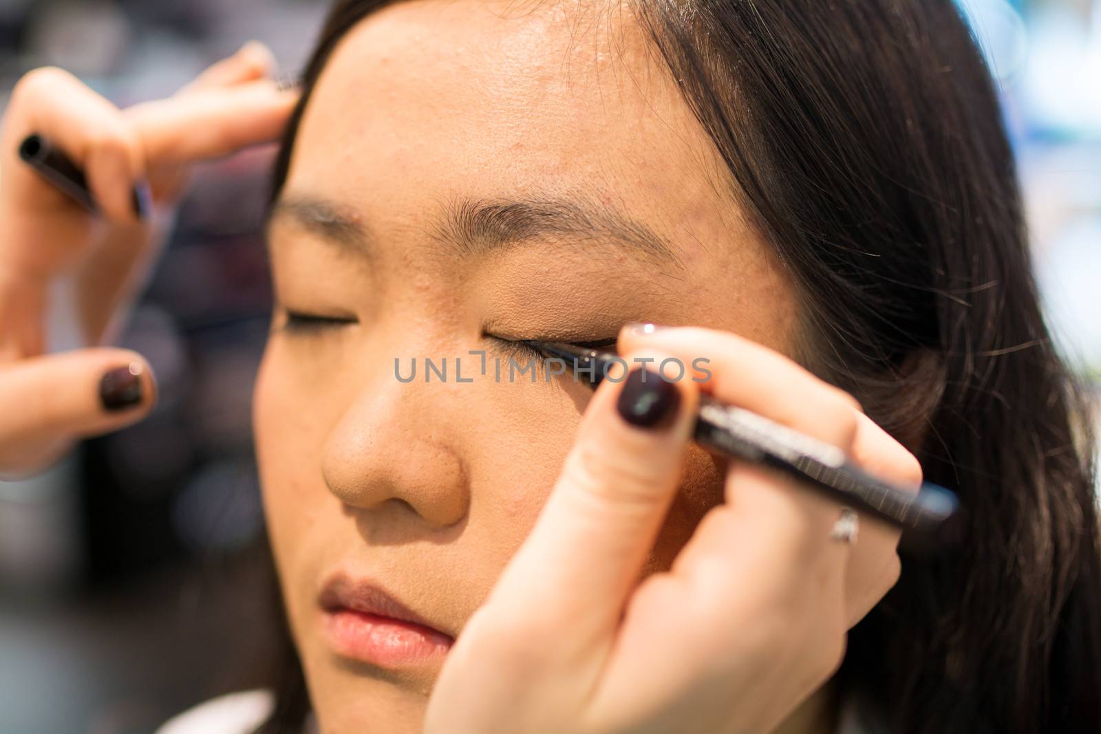 Young Asian woman applying eye liner with a small brush