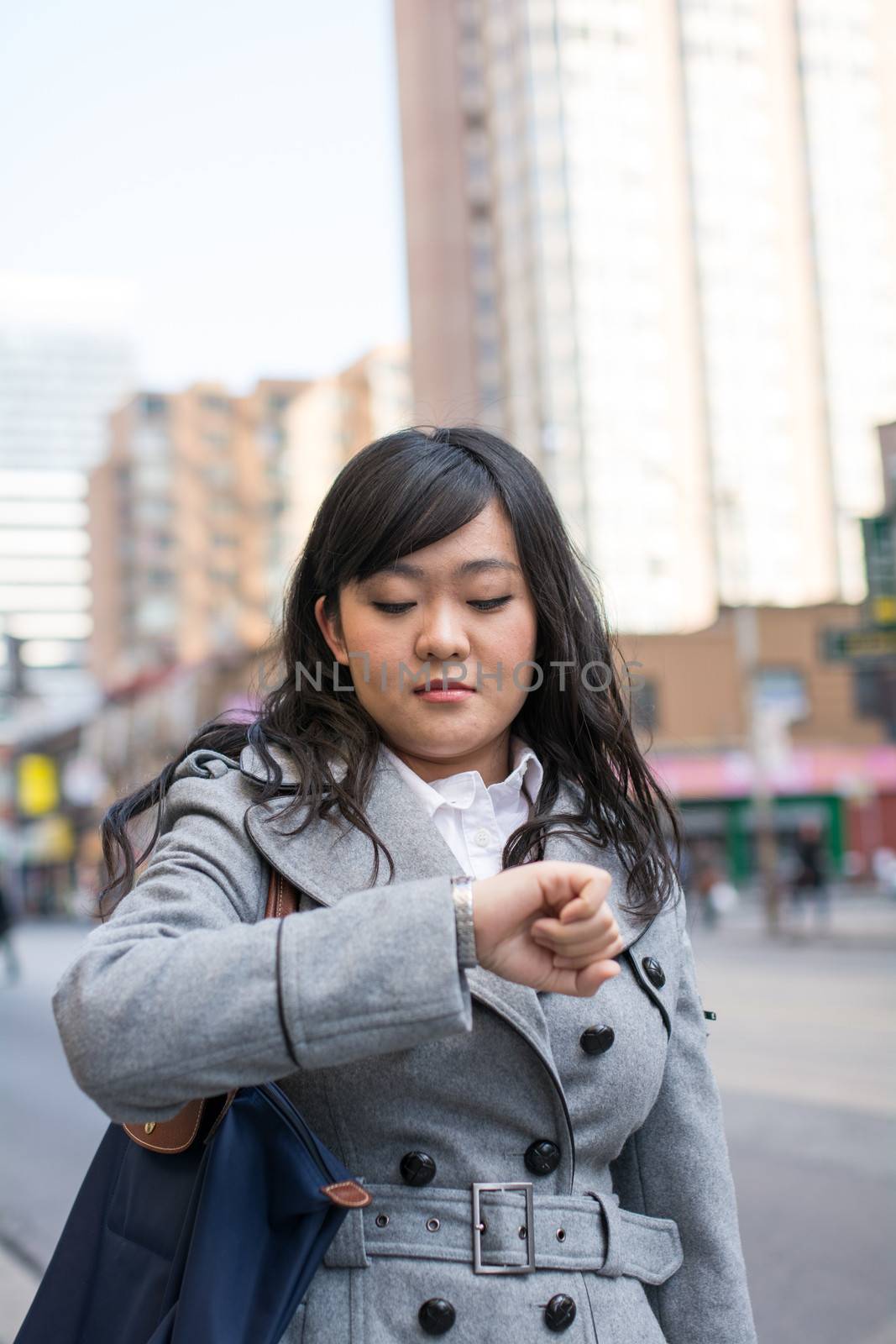Young Asian woman checking her watch on a street in a large city