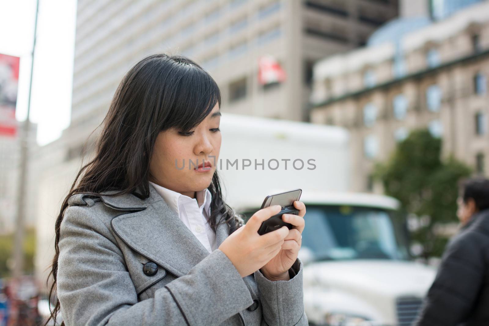 Young Asian woman texting and walking on a street in a large city