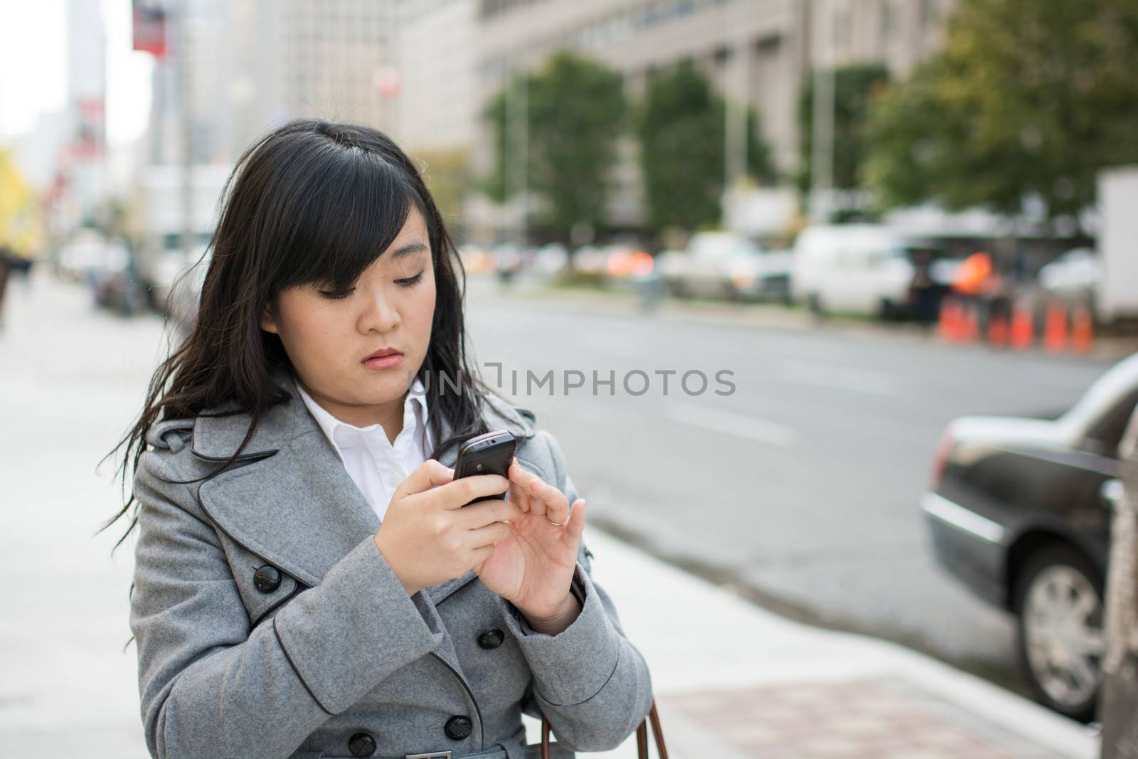 Young Asian woman texting and walking on a street in a large city