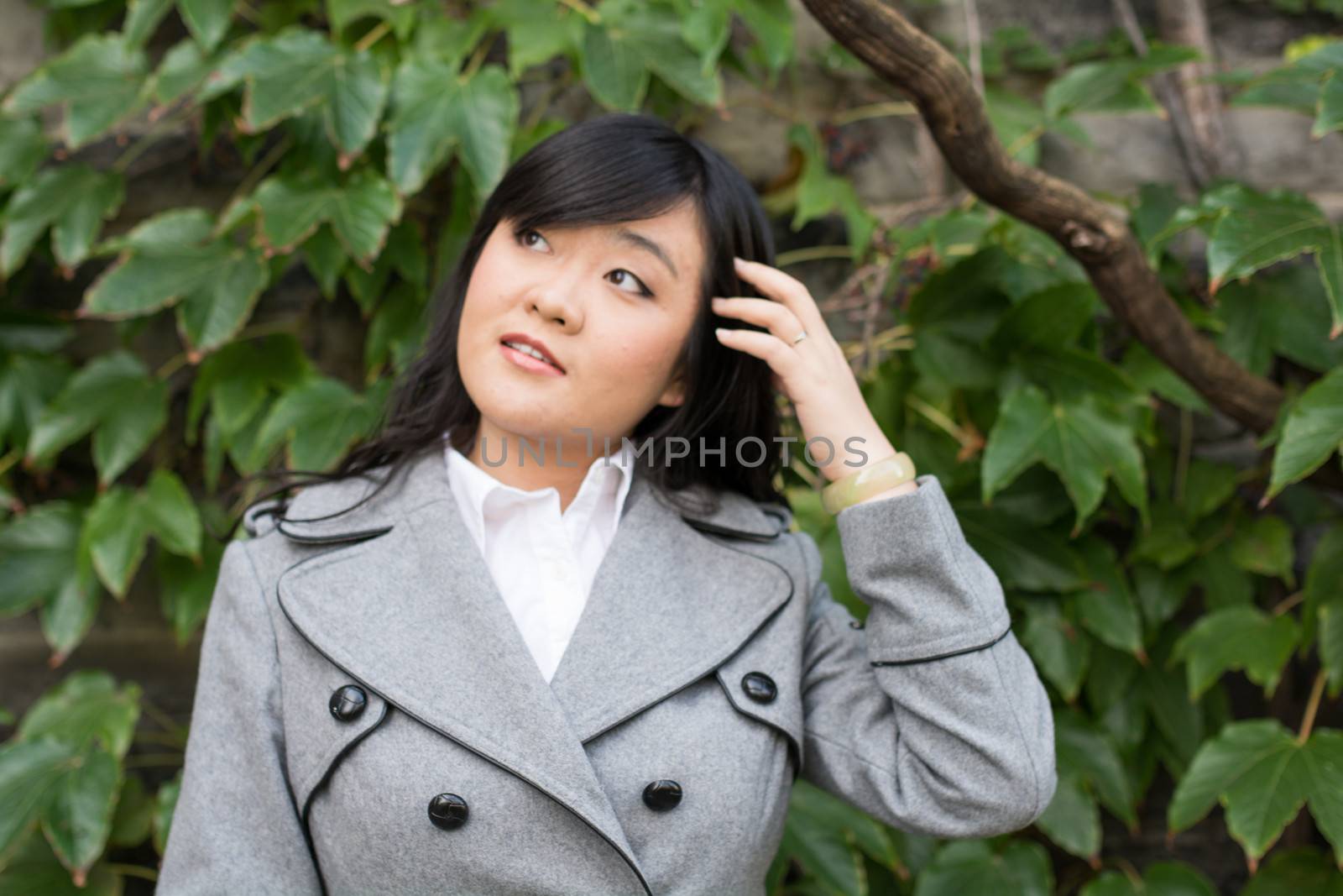 Young Asian woman standing next to leafs on a wall and smiling