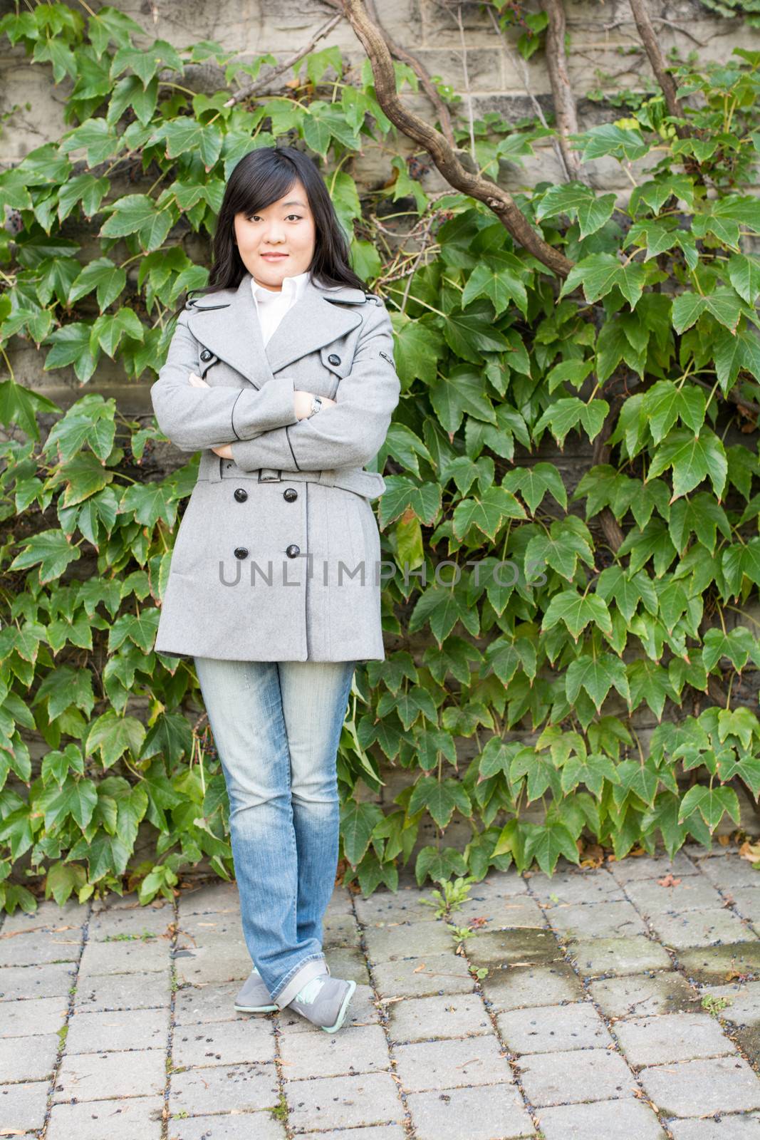 Young Asian woman standing next to leafs on a wall crossing arms