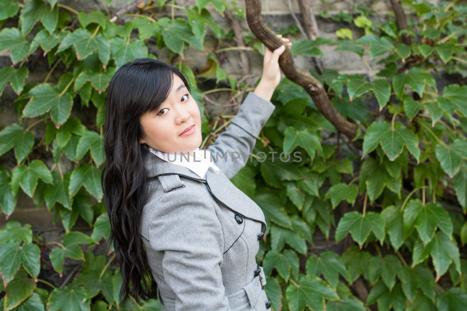 Young Asian woman standing next to leafs on a wall holding a branch