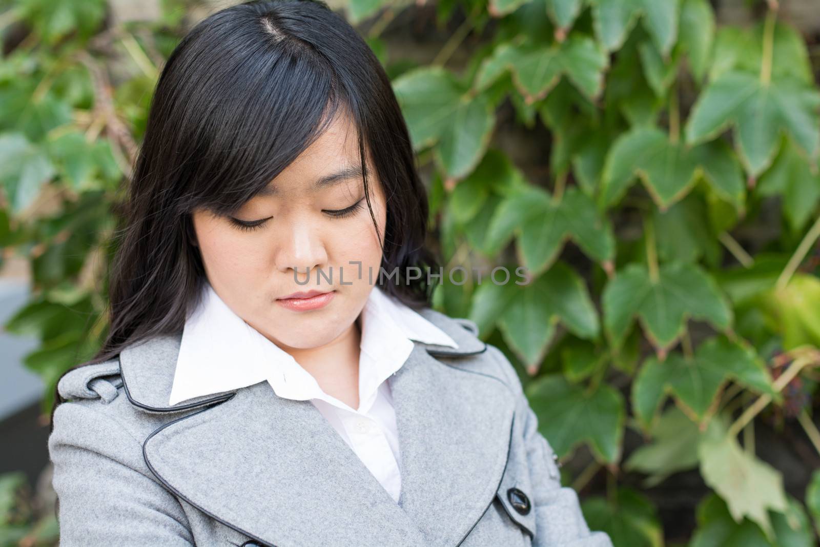 Young Asian woman standing next to leafs on a wall looking sad