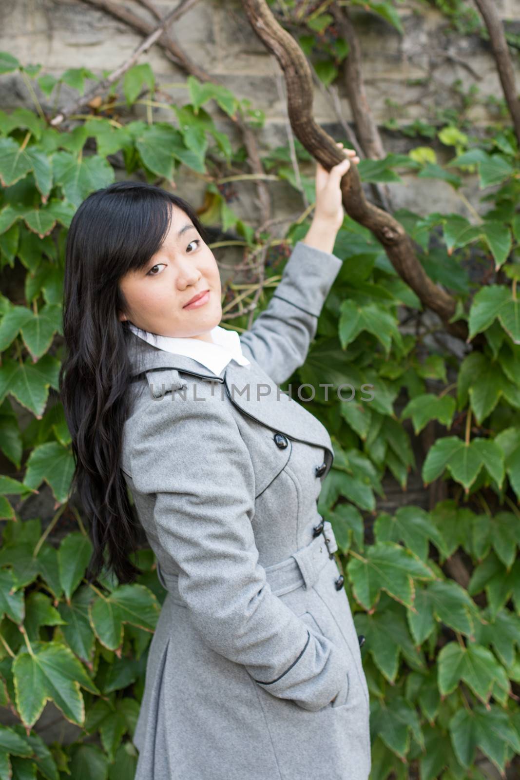 Young Asian woman standing next to leafs on a wall holding a branch