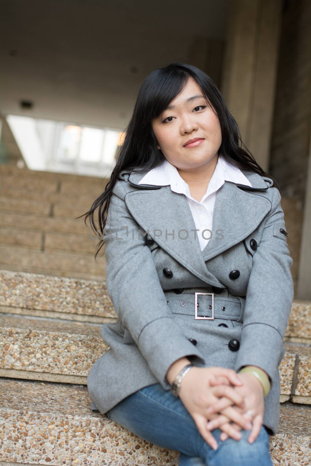 Young Asian woman in sitting on stairs in front of a business building