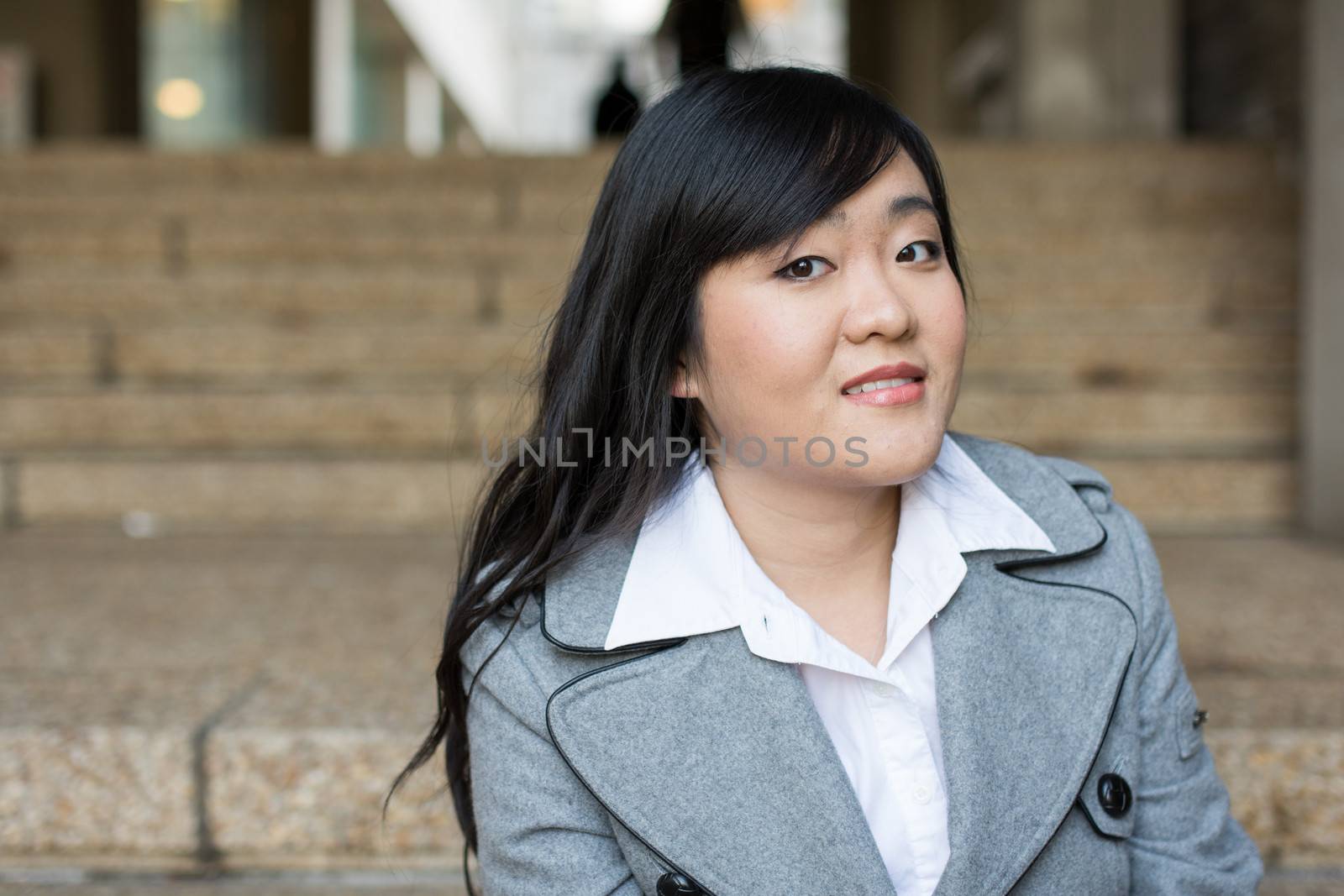 Young Asian woman in sitting on stairs in front of a business building