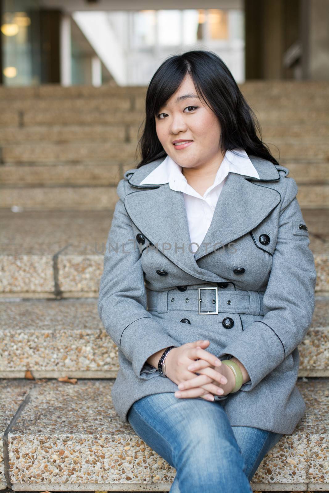 Young Asian woman in sitting on stairs in front of a business building