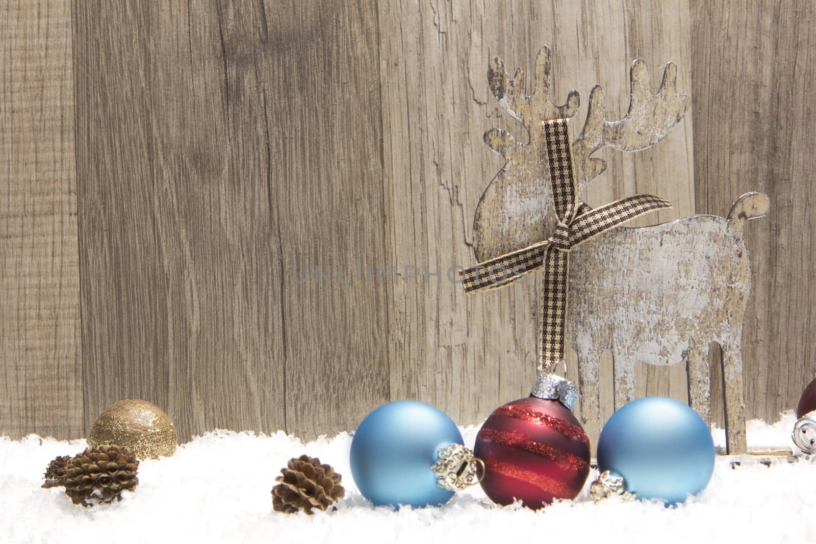 christmas decoration with wood background, snow, elk, christmas baubles gold, blue and red and pine cones 