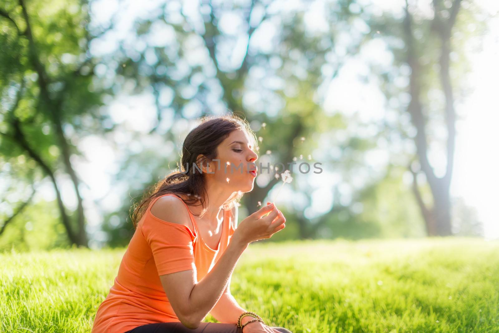 Portrait of girl in nature blowing on a dandelion at sunset