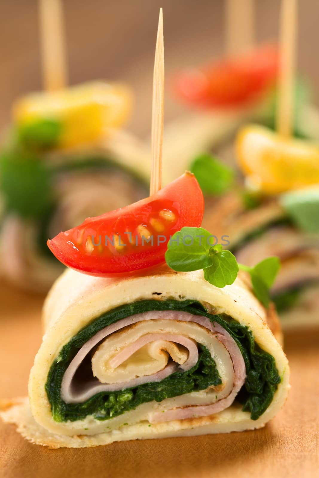 Crepe rolls as finger food filled with spinach and ham garnished with cherry tomato and watercress served on wooden board (Selective Focus, Focus on the middle of the crepe roll) 