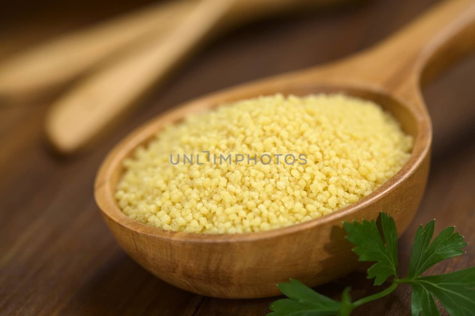 Raw couscous on wooden spoon with parsley leaf on the side (Very Shallow Depth of Field, Focus one third into the couscous)