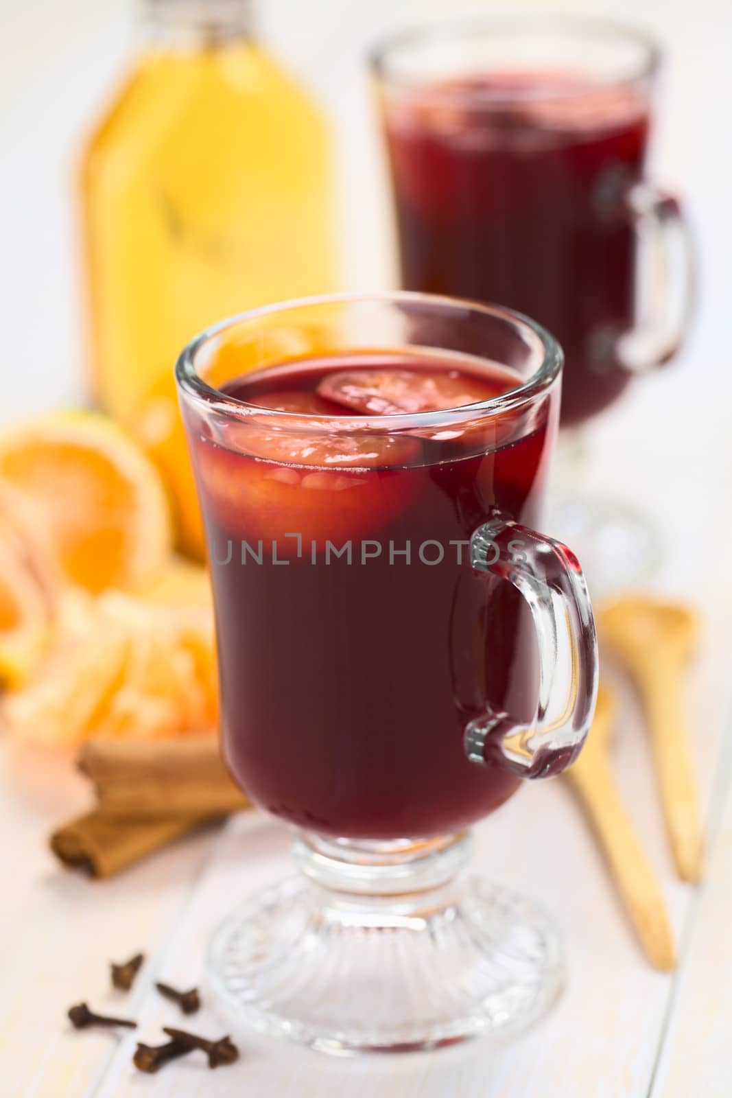 Hot spiced mulled red  wine with mandarin on top, with cloves, cinnamon sticks, mandarin, wooden spoon and a small bottle of rum (Selective Focus, Focus on the front of the rim and the handle of the glass) 