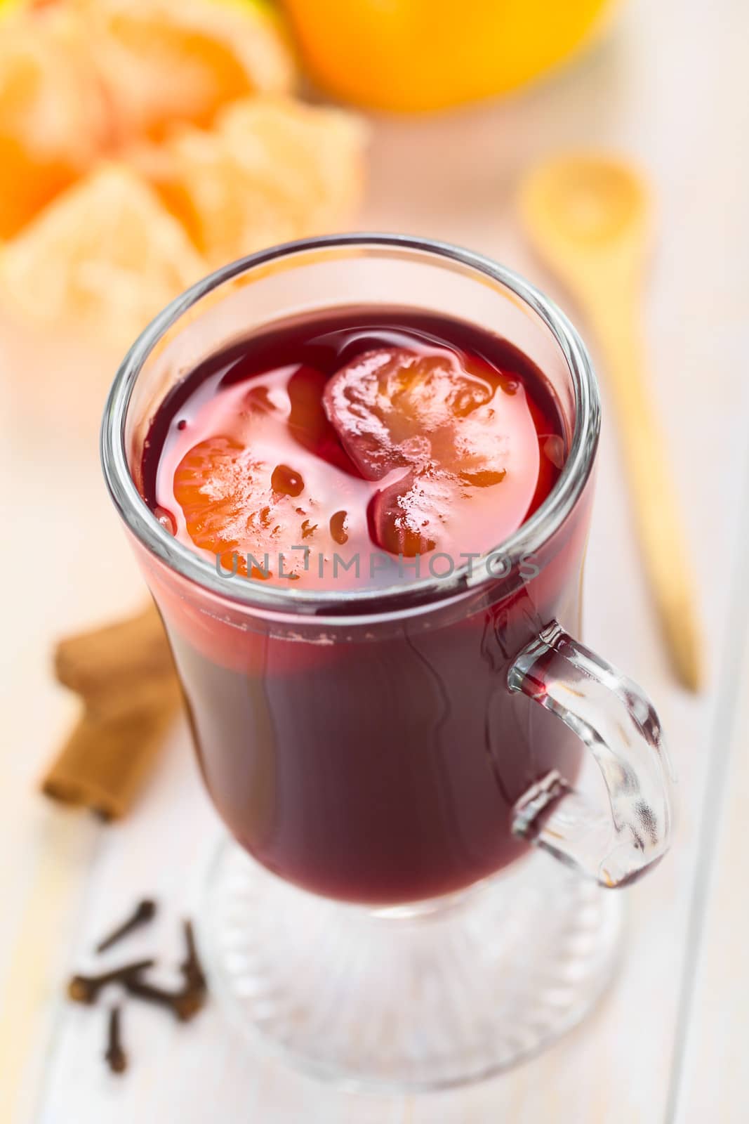 Hot spiced mulled red  wine with mandarin segments on top, with cloves, cinnamon sticks, mandarin and wooden spoon (Selective Focus, Focus one third into the mandarin segments on the drink) 