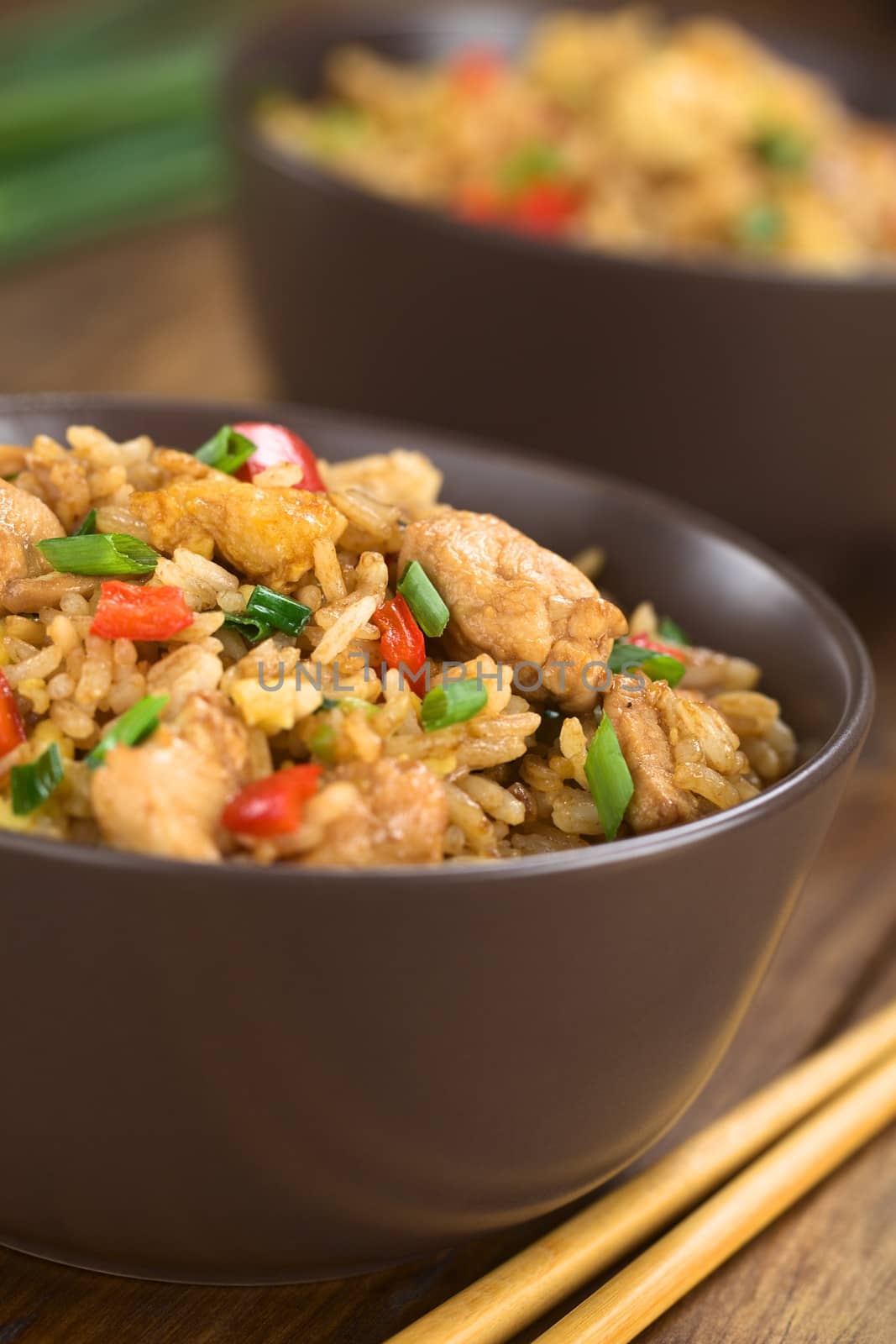 Homemade Chinese fried rice with vegetables, chicken and fried eggs served in brown bowl with chopsticks on the side (Selective Focus, Focus on the top of the dish)