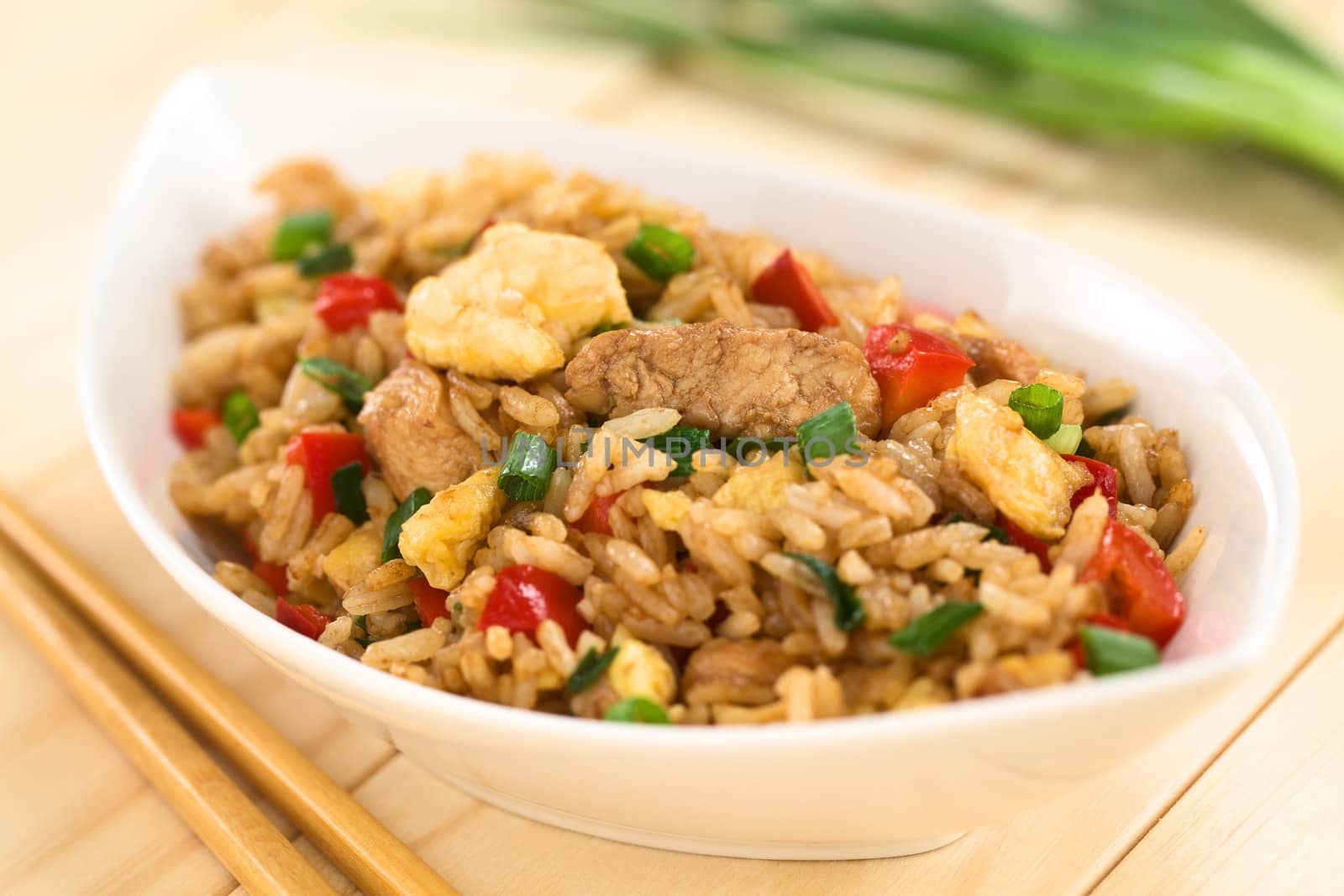 Homemade Chinese fried rice with vegetables, chicken and fried eggs served in bowl with chopsticks on the side (Selective Focus, Focus on the meat in the middle of the image)