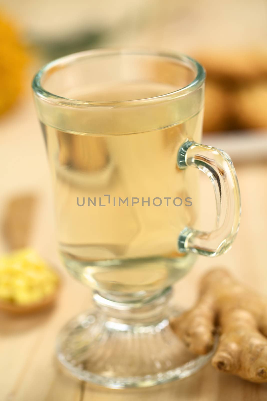 Freshly prepared hot ginger tea made of fresh ginger root served in glass (Selective Focus, Focus on the front of the rim and the handle of the glass)