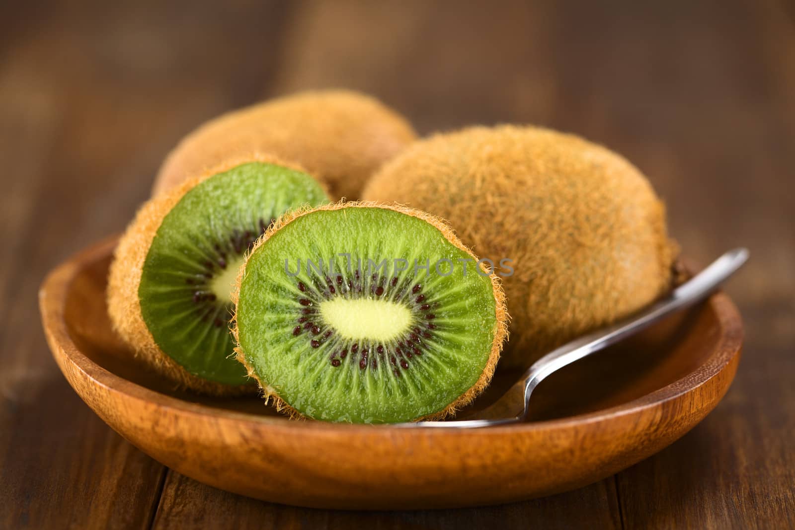 Kiwifruits on wooden plate with spoon (Selective Focus, Focus on the half kiwi)