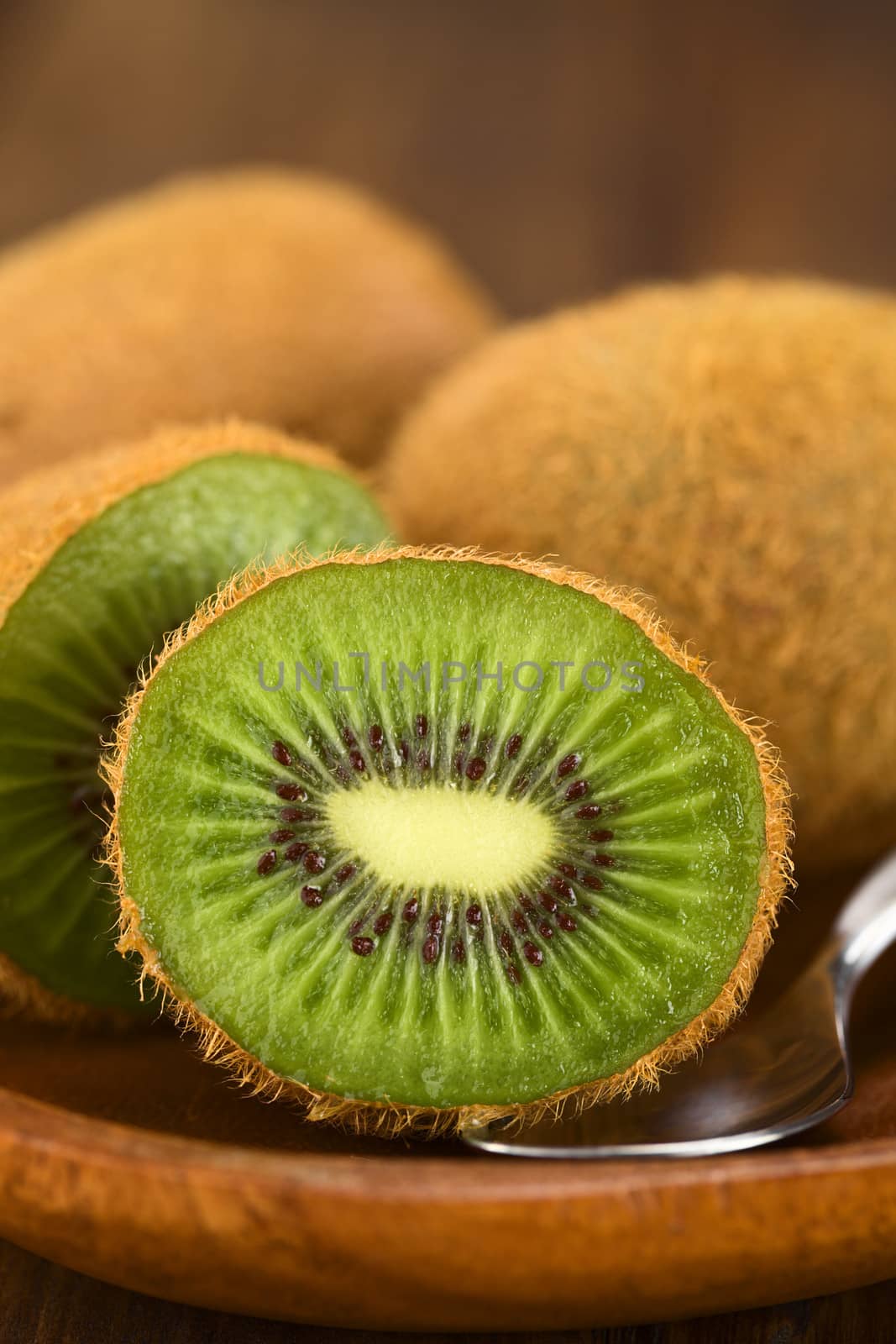 Kiwi fruits on wooden plate with spoon (Selective Focus, Focus on the half kiwi)