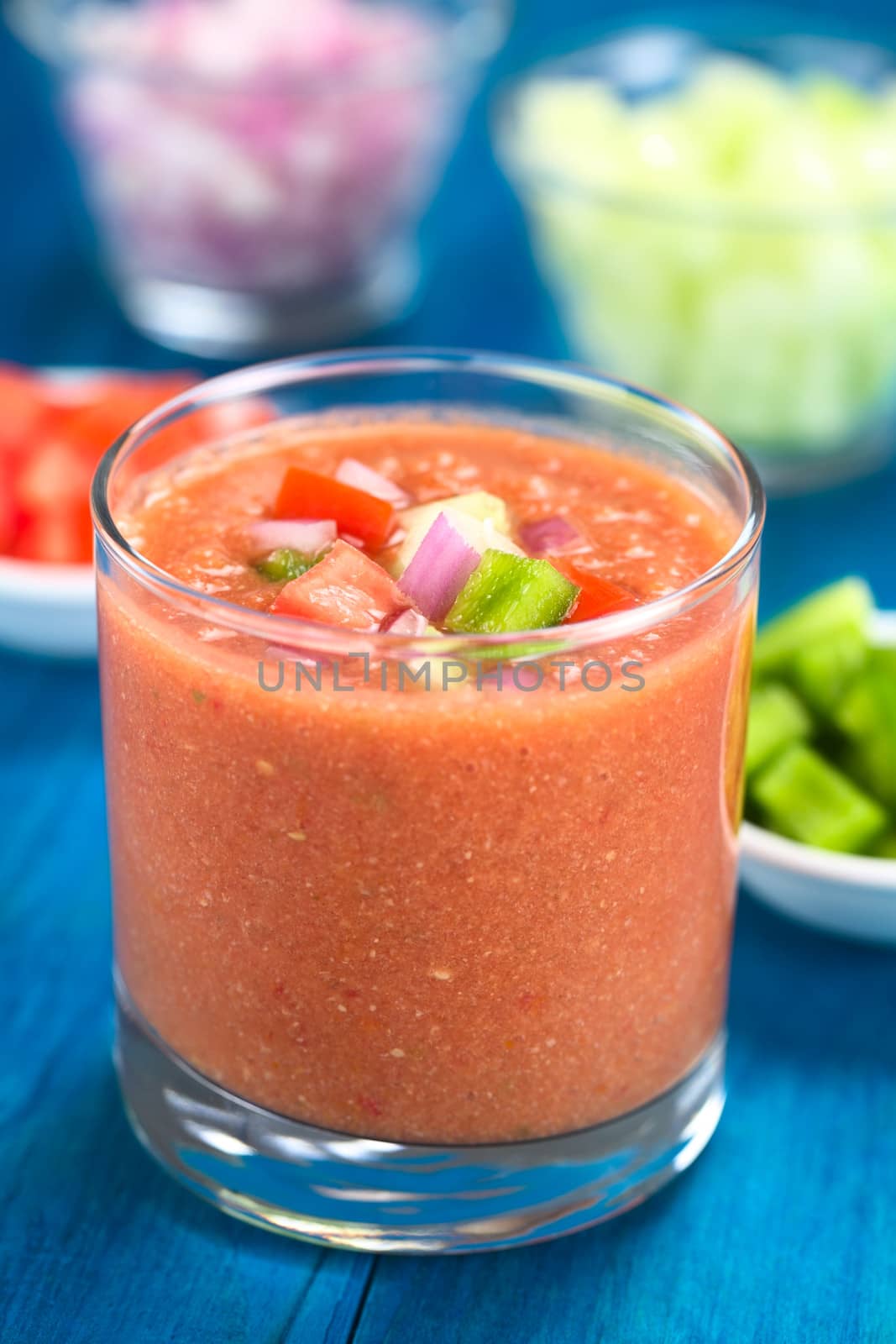Traditional Spanish cold vegetable soup made of tomato, cucumber, bell pepper, onion, garlic and olive oil served in glass (Selective Focus, Focus on the front of the vegetables on the top of the soup)