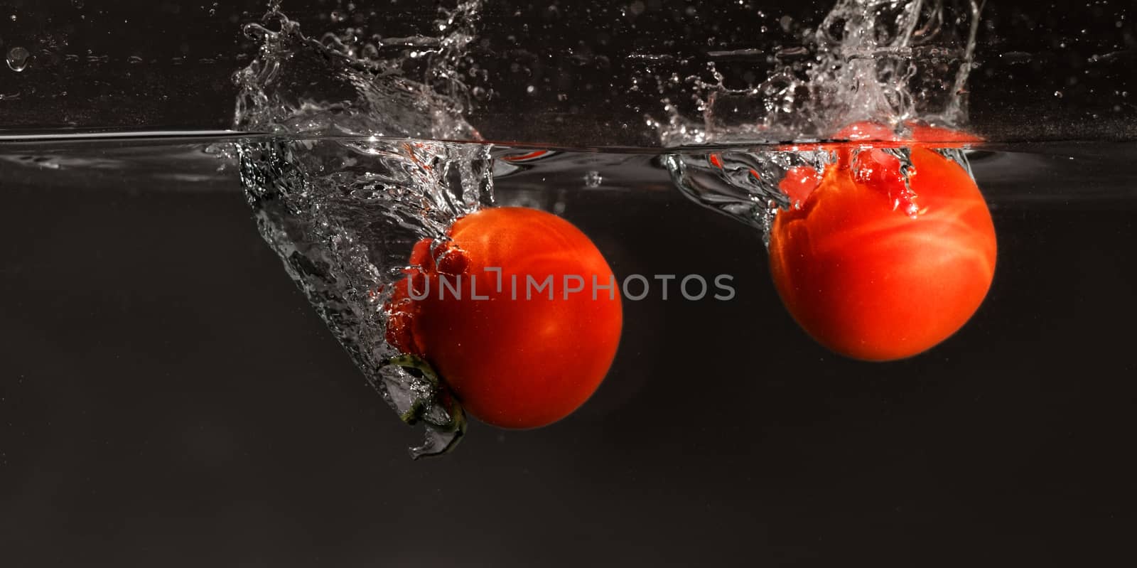 Fresh tomato dropped into water, isolated on dark background 