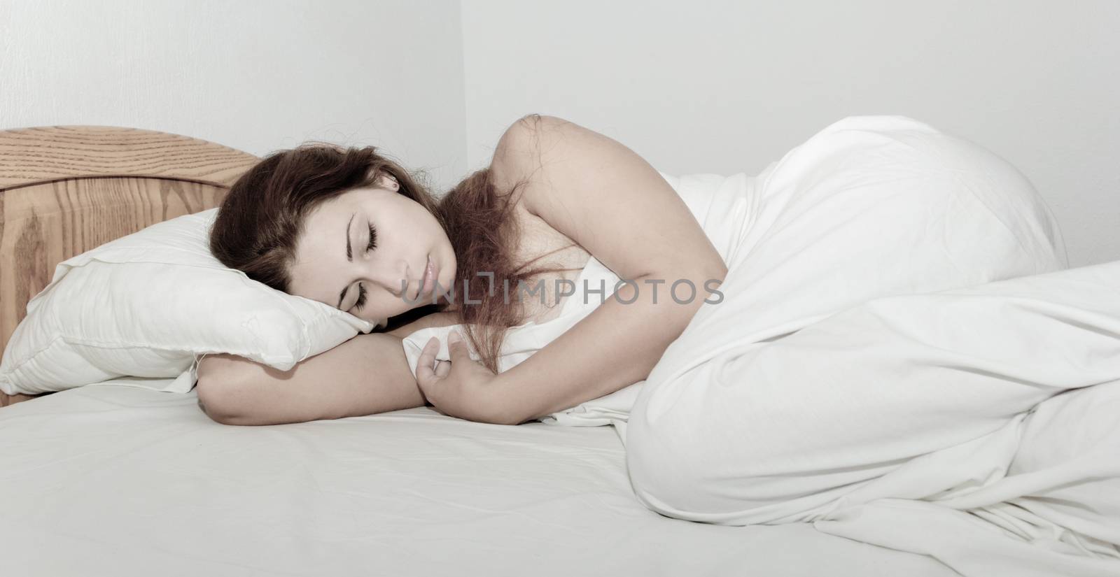 beautiful girl with long brown hair sleeping in the white bed