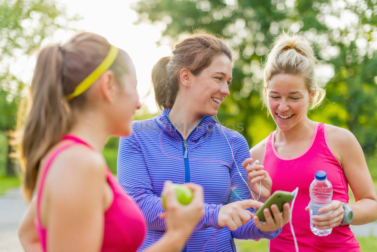 Group of happy active girls preparing for a run in nature by choosing music on smart phone