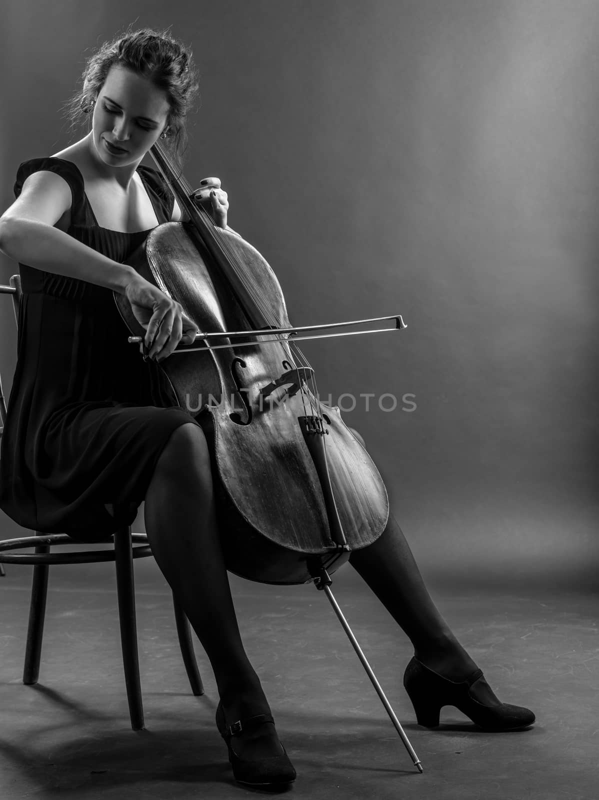 Photo of a beautiful female musician playing a cello. Black and white image.
