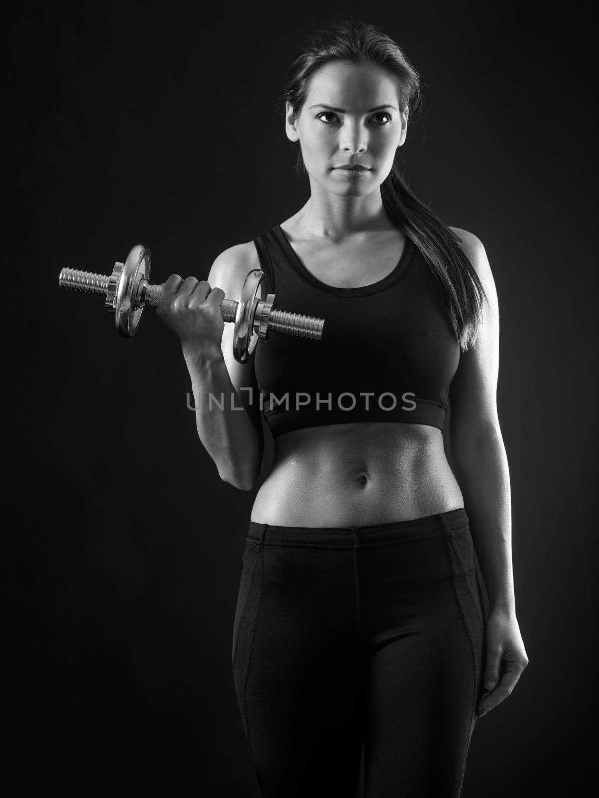 Photo of an attractive female doing a dumbbell curl black and white version.
