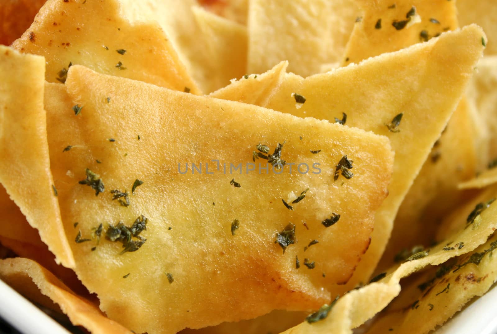 Background of assorted baked pita crisps with herbs.