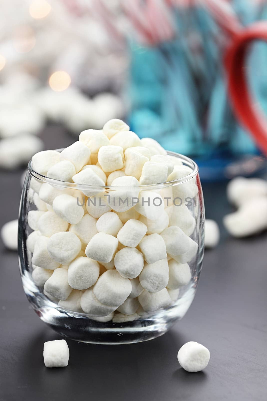 Glass of mini marshmallows with jar of candy canes and cup in background. Extreme shallow depth of field.