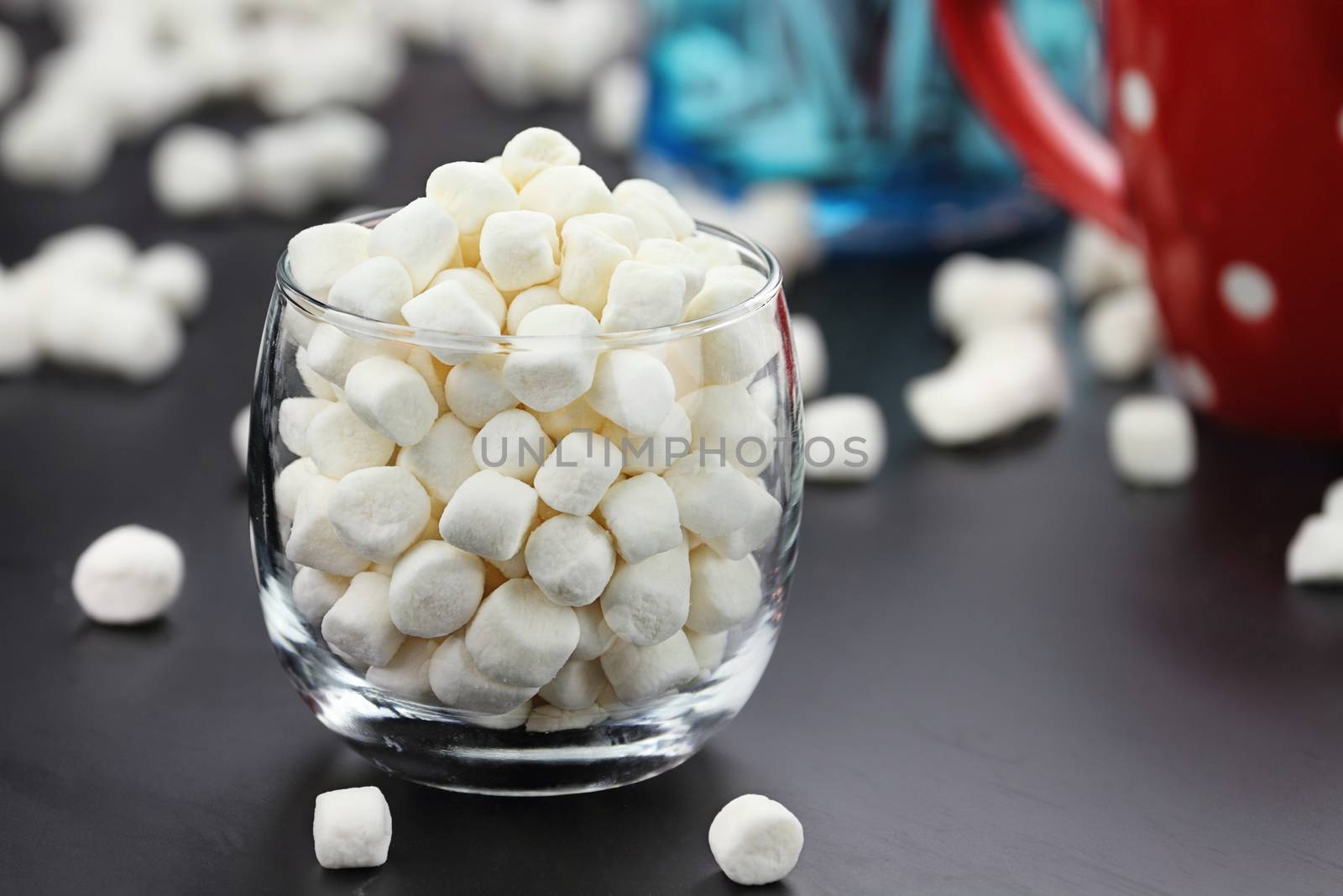 Glass of mini marshmallows with cup of cocoa in the background. Extreme shallow depth of field.