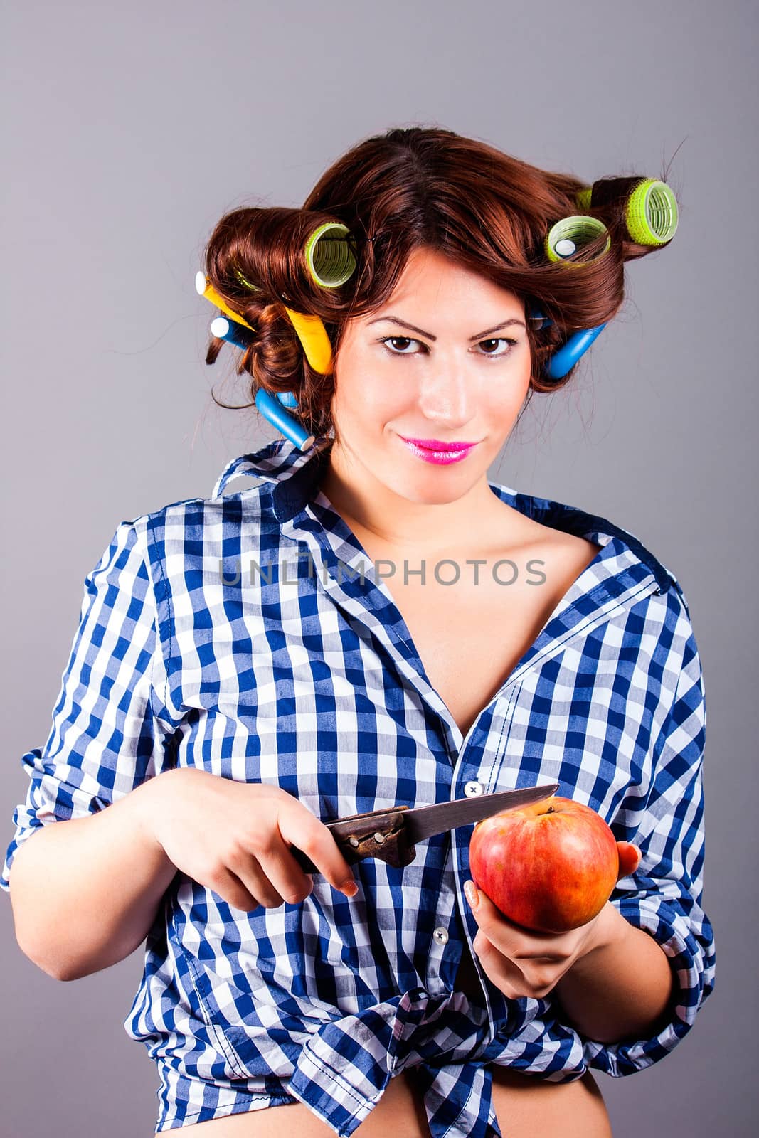 Beautiful housewife with curlers holding apple and the knife by dukibu
