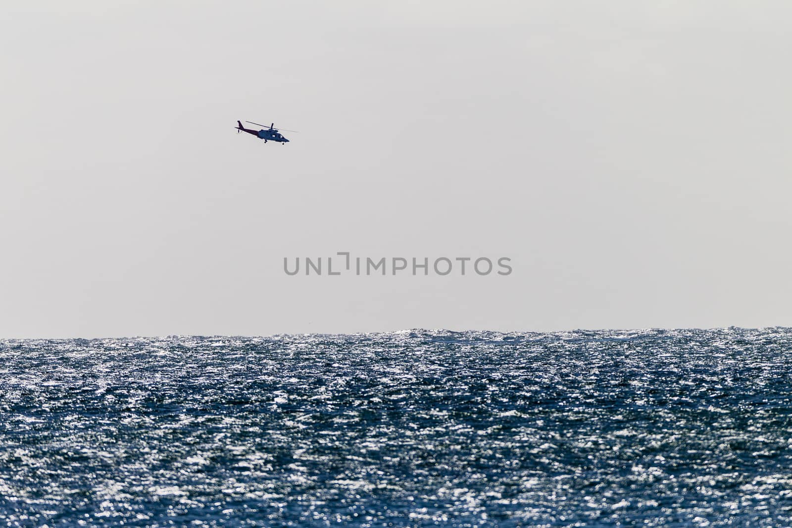 Distant helicopter flying over ocean in high storm winds making water chops on sea water.