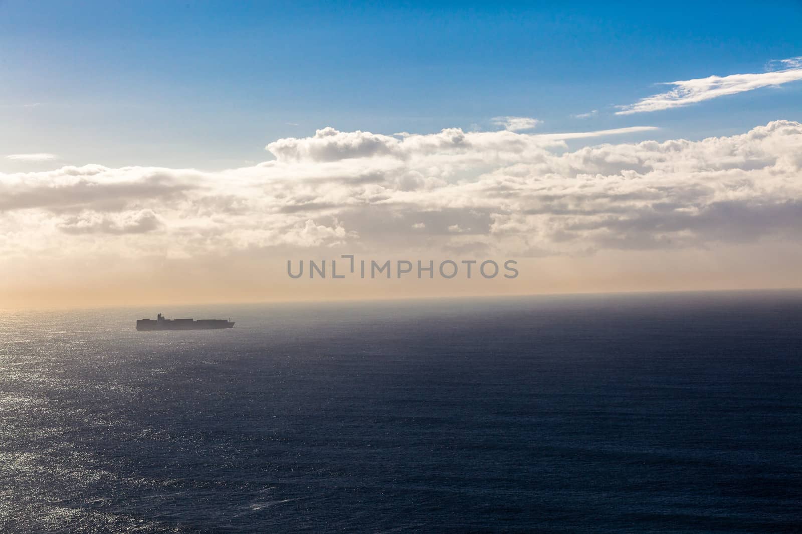 Air photo of Cargo container ship on the vast sea ocean expanse with blue horizon and cloud detail.