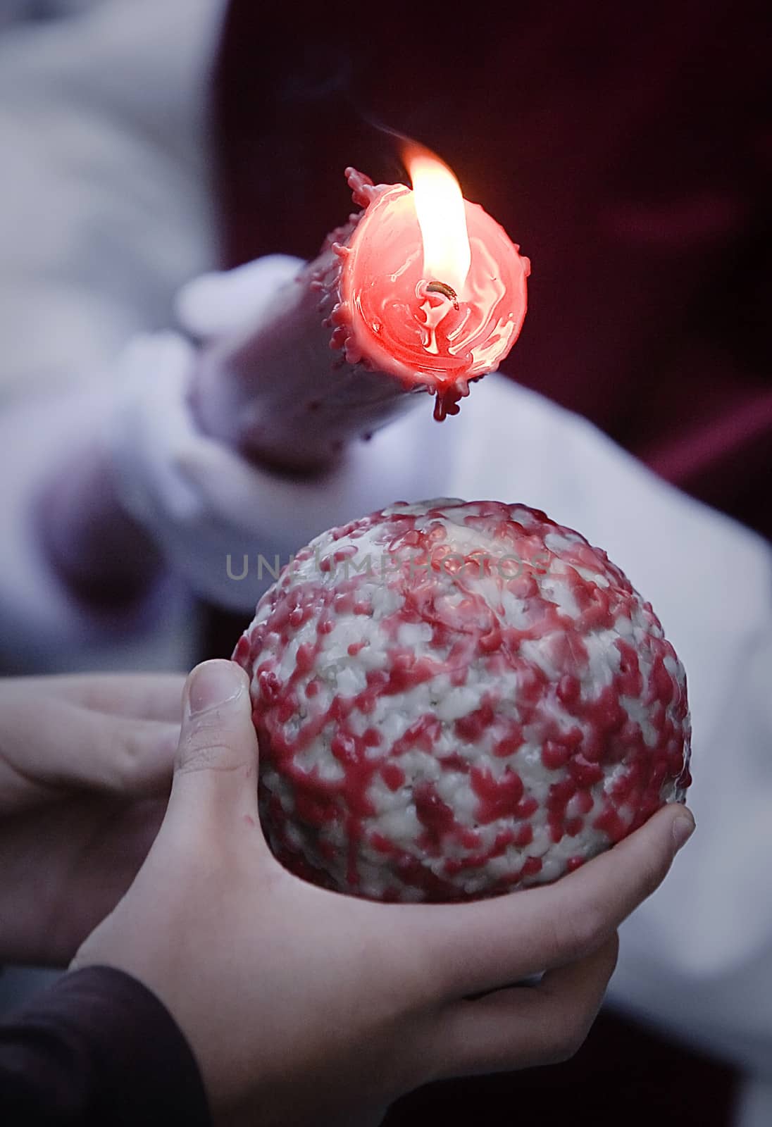 Detail penitent red holding a candle pouring wax on a ball that holds a child in the hand during Holy Week, Spain